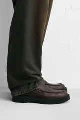 Mocasín de cuero color marrón oscuro, con antifaz y suela track de goma negra.