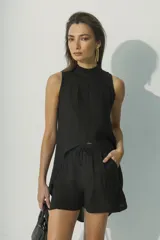 Top sin mangas blanco con cuello alto y bajo asimétrico, de textura arrugada.