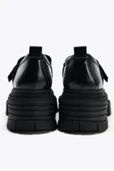 Zapato tipo mocasín negro con plataforma y suela track. Presenta tira ajustable adherente y tirador trasero.