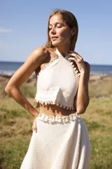 Top halter de lino color crudo, con escote enmarcado por bordes festoneados y tiras cruzadas en la espalda.