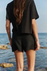 Short negro de tiro alto confeccionado en lino y rayón, con cierre invisible y doble botón lateral.