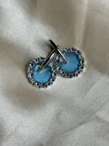 Par de aros colgantes con argolla de acero quirúrgico, dije circular de resina negra y borde de strass plateado.