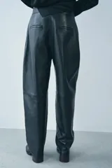 Pantalón de cuero negro de tiro medio, con pinzas delanteras, bolsillos laterales ocultos y corte holgado.
