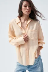 Camisa color durazno confeccionada en algodón, de corte amplio, con cuello solapa, manga larga con puños abotonados, hombros caídos, bolsillo de parche en el pecho, pinzas en la espalda y cierre frontal con botones.