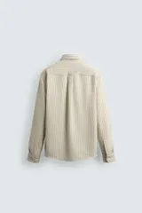 Camisa de hombre relaxed fit confeccionada en tejido de algodón a rayas verticales color beige y marrón. Tiene cuello solapa, manga larga con puños abotonados, bolsillo de parche en el pecho y cierre frontal con botones.