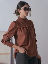 Blusa marrón con cuello alto fruncido y mangas largas abullonadas con puños elásticos fruncidos.