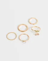 Set de 5 anillos dorados de metal con diferentes diseños: uno torzado, uno con strass, uno con dije de cerezas con strass de colores, uno con strass engarzado y uno liso.