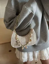 Cartera tipo baguette de paja color beige, con forro blanco, asa de cadena dorada y apliques de perlas y conchas marinas.