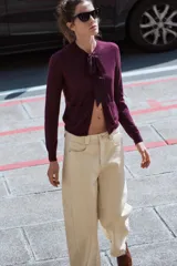 Chaqueta color borgoña de tejido de punto con lana y alpaca. Tiene cuello redondo con lazo de satén, manga larga y cierre frontal con botones. Presenta dos bolsillos de parche en el frente.