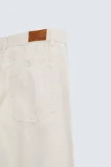 Pantalón de jean color beige, corte recto y relajado, con cintura ajustable con cordón interior, cinco bolsillos, efecto lavado y cierre frontal con cremallera y botón.