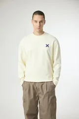 Buzo de manga larga color crema claro, con cuello redondo y un pequeño logo bordado en forma de 'X' de color azul marino en el pecho.