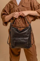 Cartera mochila color tostado, símil cuero, con compartimiento principal amplio y bolsillos frontales con cierre. Tiene correas ajustables para usar como mochila y asa superior para llevar al hombro.