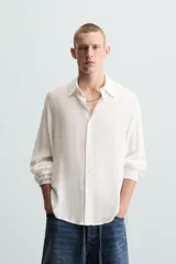 Camisa de hombre color blanco, de manga larga y cuello solapa, con un patrón jacquard sutil a cuadros. Presenta un calce relajado (relaxed fit) y bajo con aberturas laterales.