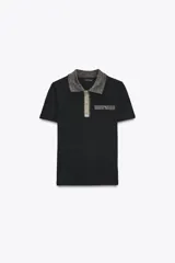 Chomba negra de corte slim fit, con cuello polo y mangas cortas. Presenta un falso bolsillo en el pecho y cierre frontal con botones. Detalle de hilo metalizado en cuello, bolsillo y tapeta.