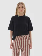 Remera de punto negra con cuello redondo y mangas cortas. Presenta un diseño de tejido con trenzas verticales.