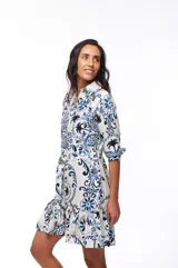 Vestido corto con estampado floral en tonos azules y negros sobre fondo blanco, corte camisero con cuello clásico, mangas 3/4 y falda con volantes.