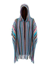 Poncho de tejido de punto con capucha y cierre frontal. Presenta el icónico patrón de zigzag (chevron) en múltiples colores vibrantes como azul turquesa, naranja, rosa, negro y beige. El borde inferior tiene flecos.