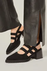 Zapato cerrado de cuero negro, con punta fina, taco ancho y plataforma con suela de goma dentada. Presenta tiras de sujeción cruzadas en el empeine y una tira elástica en el talón.