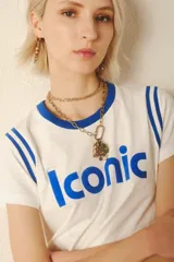 Remera blanca de algodón con cuello redondo y mangas cortas con ribetes azules. Estampado frontal con la palabra "Iconic" en color azul.