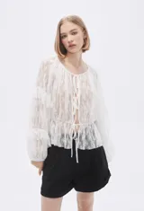 Blusa blanca traslúcida de encaje con mangas largas abullonadas y volados.