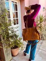 Bolso de mano grande de cuero color marrón, con doble asa corta y correa larga desmontable. Tiene cierre superior y detalles de flecos en el frente.