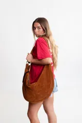 Cartera hobo grande de cuero descarne color marrón, con correa de hombro ajustable y cierre superior con cremallera.