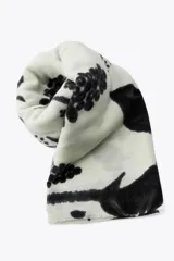 Pañuelo rectangular de color crema con estampado de ramas y flores en negro. Tiene terminaciones deshilachadas.