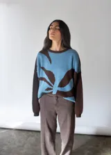 Sweater oversize tejido en punto jersey color celeste con mangas marrones y diseño de hoja abstracta en el frente.