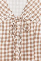 Vestido corto de escote pico con cuello bobo y manga sisa. Detalle de flores bordadas y entredoses. Forro interior. Cierre frontal con botones forrados y lazada. Estampado a cuadros vichy color marrón y blanco.