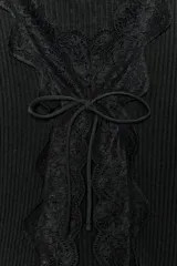 Top negro de tejido acanalado (rib) con escote pico y manga larga. Presenta una aplicación de encaje negro a tono que forma un lazo frontal ajustable.