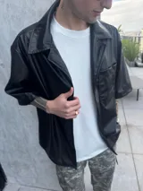 Camisa negra de cuerina, corte boxy, manga corta y cuello clásico.