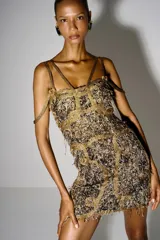 Vestido corto con textura artesanal en hilos metálicos y bordados dorados sobre base negra. Presenta tiras finas que cruzan sobre los hombros y un diseño ceñido al cuerpo.