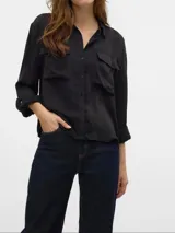 Camisa negra de corte clásico, con cuello, mangas largas con puños abotonados, cierre frontal con botones y dos bolsillos de parche en el pecho.