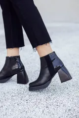 Botinetas negras de cuero con caña baja, cierre lateral y detalle de cuero texturizado en el talón. Taco geométrico y punta cuadrada.