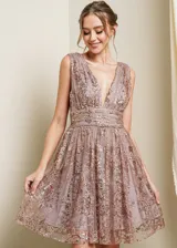 Vestido mini de fiesta color lila con escote en V profundo, sin mangas y falda acampanada. Presenta apliques de lentejuelas doradas formando un diseño floral.