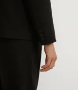 Blazer negro de poliéster y viscosa, de corte alargado, con cuello solapa, manga larga, doble botón frontal y bolsillos con solapa.