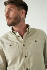 Camisa de hombre color marrón con efecto stone wash, fit regular, cuello americano, cierre con botones, dos bolsillos frontales con botón y mangas largas con puños abotonados.