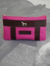 Sobre tipo cartuchera color borgoña, de lona con terminaciones en cuero marrón. Tiene cierre superior y aplique de cuero con el logo de la marca.