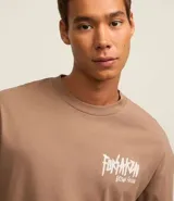Remera marrón de algodón con efecto desteñido, corte relajado, cuello redondo, mangas cortas y estampa de calaveras con texto "Forsaken Born Freak".