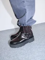 Botas de cuero color bordó con elástico en los laterales, detalle de bordado en hilo rojo en la puntera y hebillas con apliques metálicos. Plataforma de goma negra de 5 cm de altura.