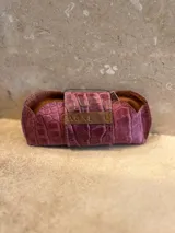 Estuche para lentes con textura símil cocodrilo color azul y cierre con tira de cuero marrón con el logo de la marca.