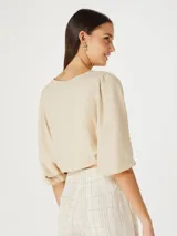Blusa beige con escote en V, mangas 3/4 abullonadas y cierre frontal con botones.