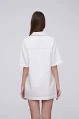 Vestido corto blanco de corte recto, con cuello camisero, escote en V, mangas cortas y dos bolsillos frontales.