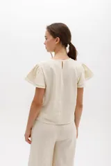 Blusa celeste de lino con bordado en relieve de formas orgánicas y terminaciones desflecadas.