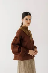Blusa color ladrillo con cuello alto de crochet y lazos para ajustar. Mangas largas abullonadas con puños elásticos.