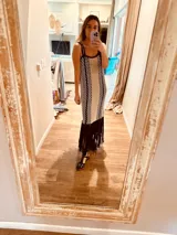 Vestido largo tejido en lurex color beige con diseño vertical y terminación en flecos negros. Breteles finos de cuero intervenido a mano con tientos de cuero plateado.