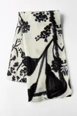 Pañuelo rectangular de color crema con estampado de ramas y flores en negro. Tiene terminaciones deshilachadas.
