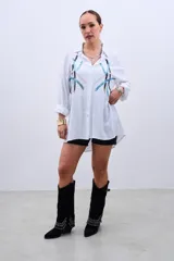 Camisa blanca de corte holgado, con cuello camisero y mangas largas. Decorada con lentejuelas de colores celeste, plateado y negro.