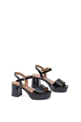 Sandalias de charol negro con plataforma y tacón cuadrado. Tira delantera ancha y tira al tobillo con hebilla dorada.