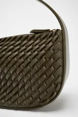 Bolso de mano color verde oliva con efecto trenzado. Tiene asa corta y correa larga extraíble. El cierre es con cremallera metálica.